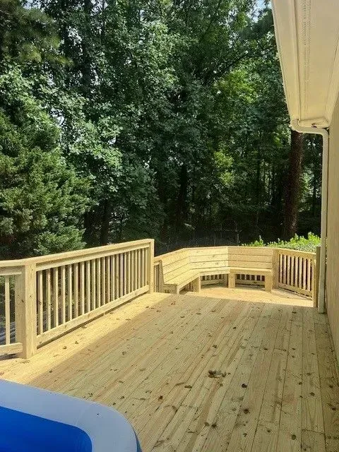 Wooden deck with beige railing overlooking a dense green wooded area