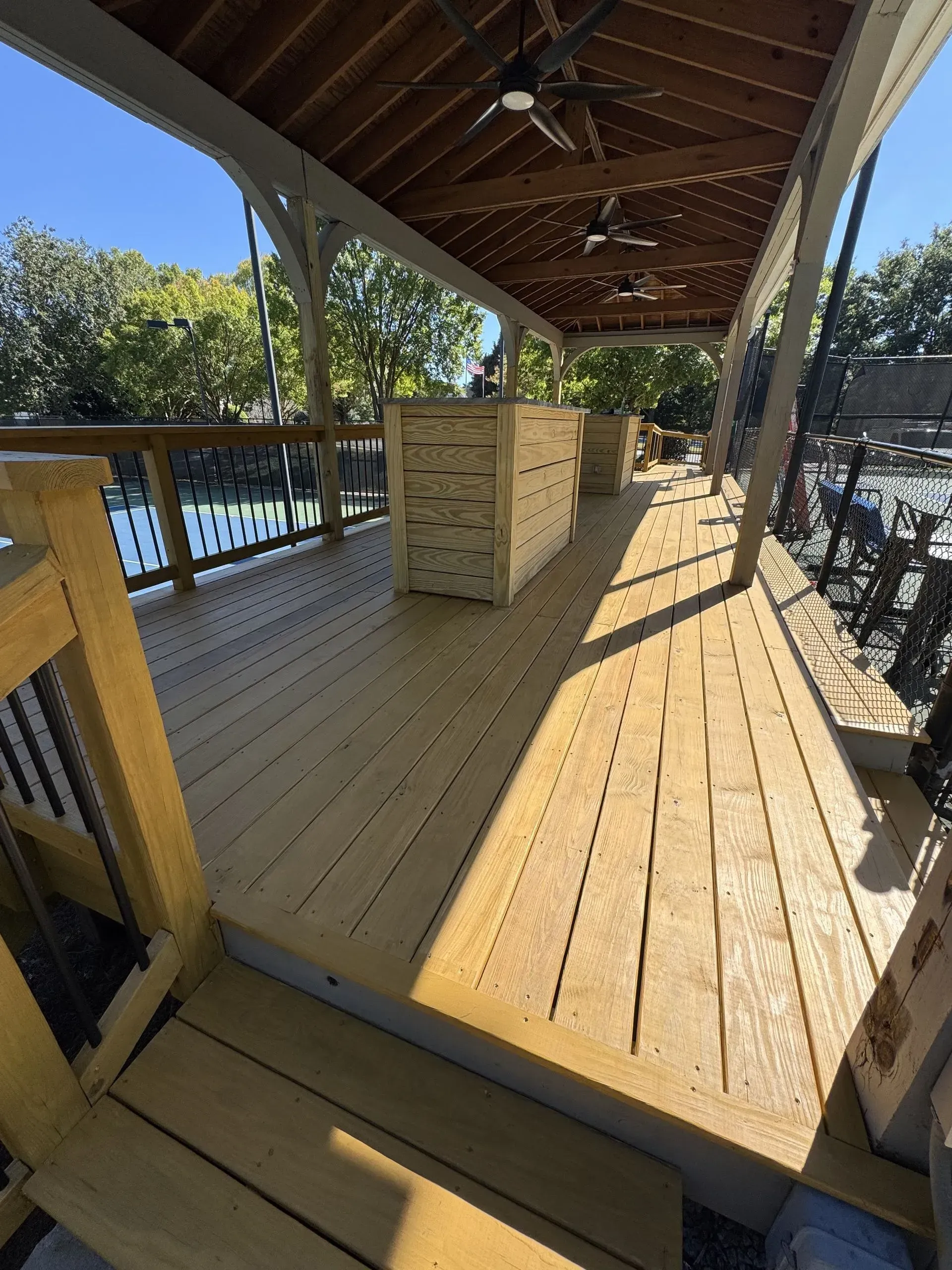Wooden deck with stacked moving boxes under a covered patio beside a fenced yard and pool