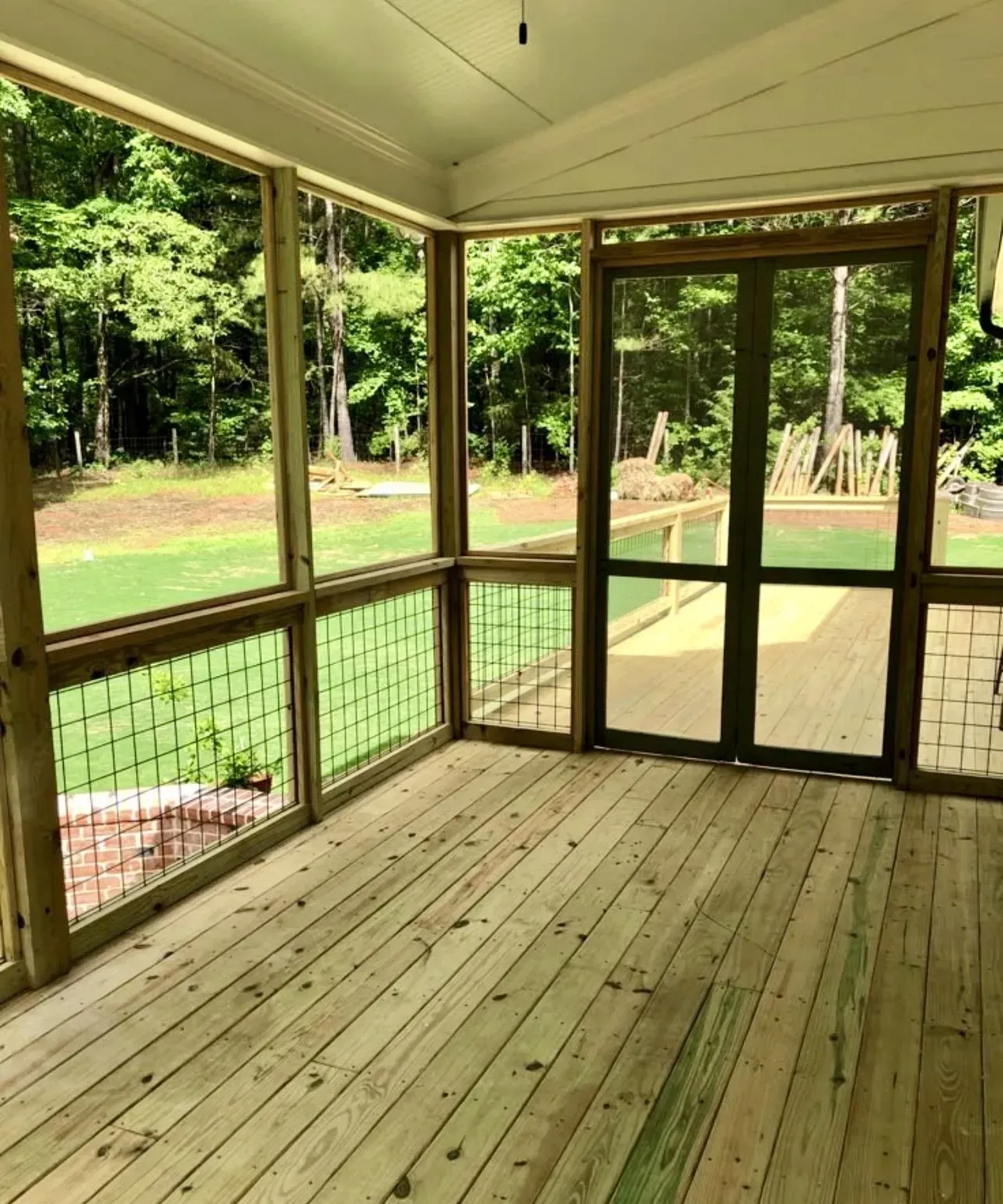 Screened porch with wooden floor and railings overlooking a green wooded yard