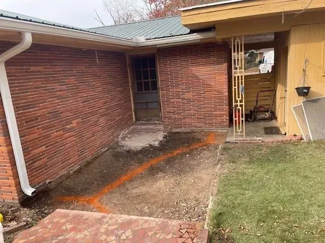 Brick house patio and walkway with concrete ramp, grass lawn, and open doorway on the right