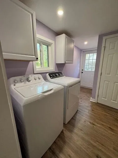 Bright laundry room with a washer, dryer, white cabinets, purple walls, and wood flooring