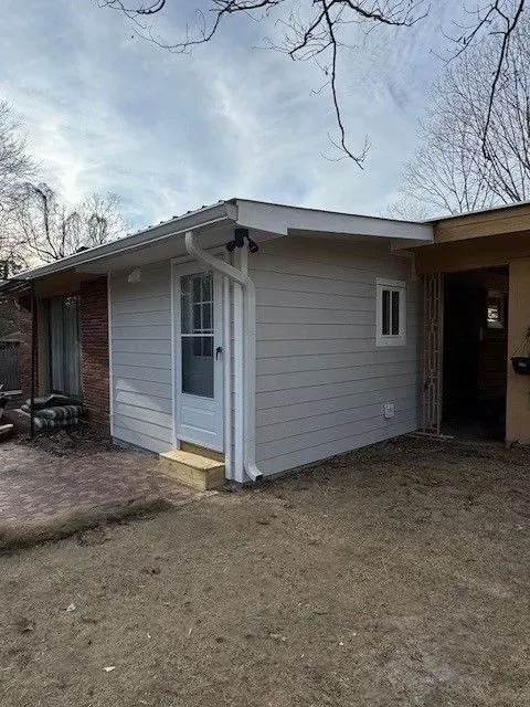 Small house exterior with white siding, gray roof, front door, and carport under bare trees.