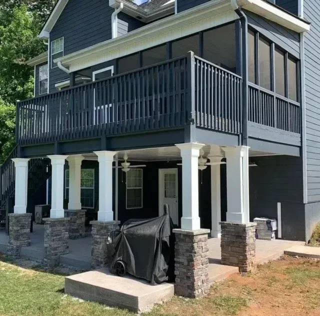 Gray house with a raised porch, white columns, dark railings, and stone steps under construction