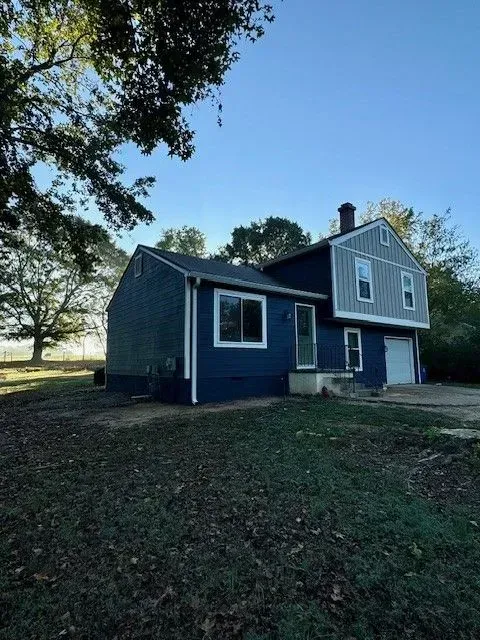Blue two-story house with white trim on a grassy lot under a clear sky