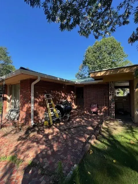 Brick house patio with ladder, motorcycle, and trees casting shadows on a sunny day