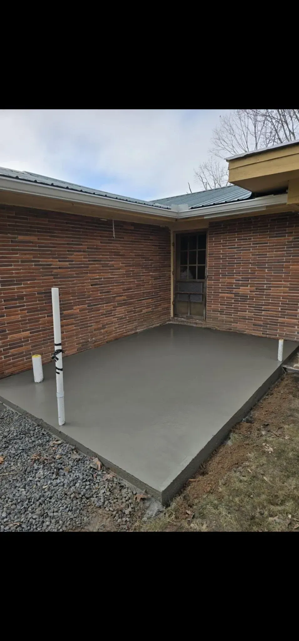 Empty concrete patio beside a brick house with a narrow doorway and gravel edging