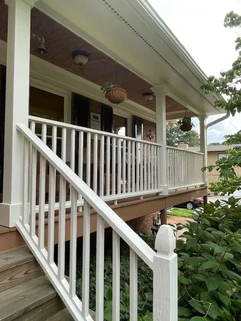 Front porch with white railings, hanging planters, and a wooden staircase under a house roof.