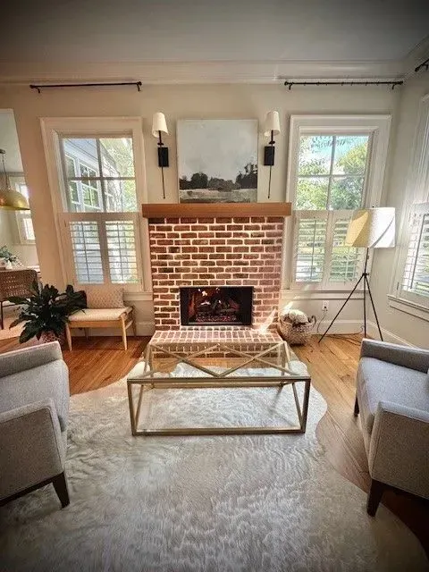 Bright living room with brick fireplace, large windows, and neutral chairs on a shag rug