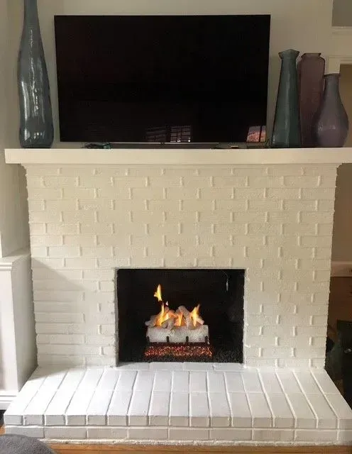 White brick fireplace with a lit fire and a TV on the mantel, flanked by decorative vases.