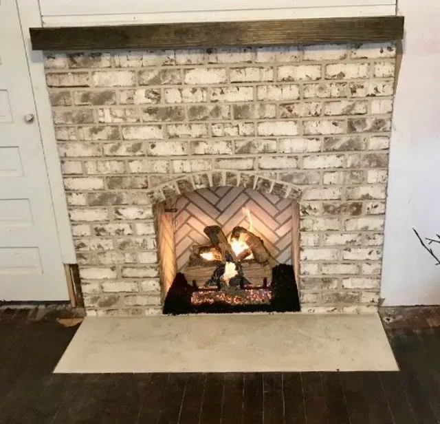 White brick fireplace with a lit fire, dark wood mantel, and beige hearth in a room with dark flooring.