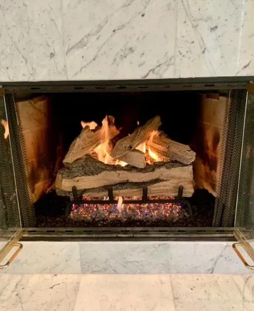 Lit fireplace with burning logs and glowing embers behind a black metal screen.