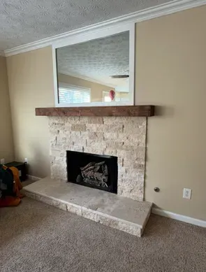 Living room fireplace with stone surround, wooden mantel, and large mirror above on beige walls.