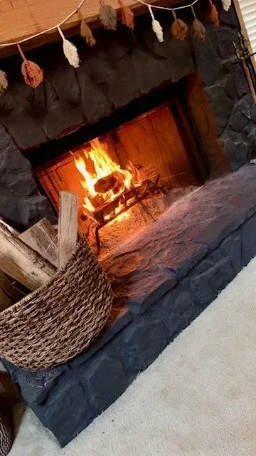 Lit fireplace with a burning fire, black stone surround, and a wicker basket on the hearth.
