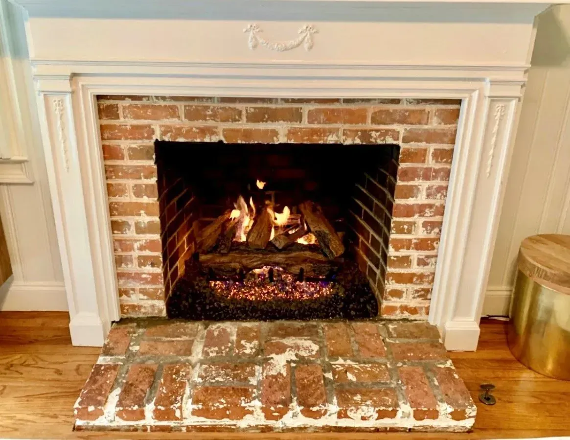 Lit brick fireplace with a white mantel and hardwood floor in a cozy room
