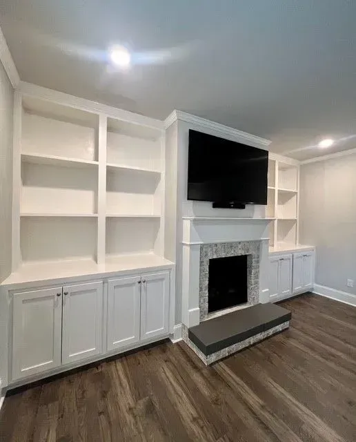 Living room with built-in white shelving, a fireplace, wall-mounted TV, and dark wood floors.