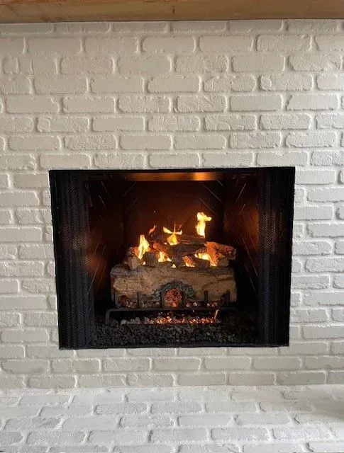Lit fireplace set into a white painted brick wall with a warm orange glow.