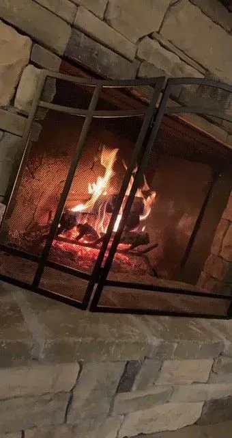 Lit fire in a stone fireplace with a black metal screen in front