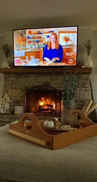 Living room with a lit fireplace, TV above mantel, and a wooden baby play area in front