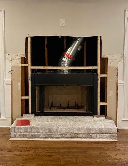 Unfinished fireplace wall with exposed framing and metal vent pipe above a black firebox.