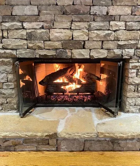 Stone fireplace with a lit fire behind glass doors, glowing orange embers and logs.