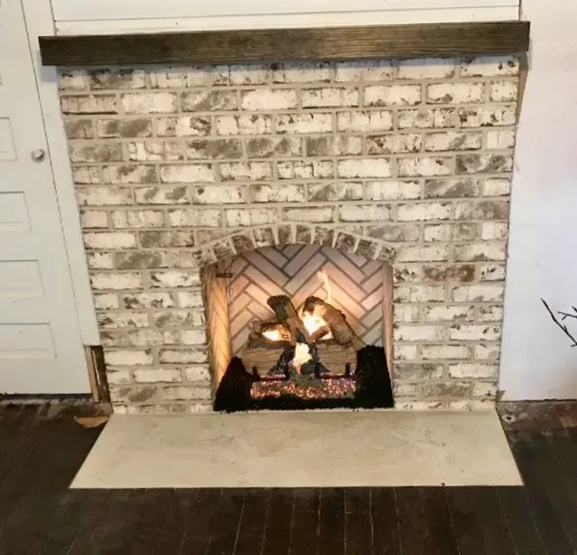 White brick fireplace with a lit fire and beige hearth in a room with dark wood floors