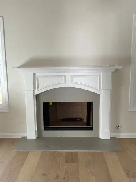 White fireplace with mantel in a beige room, centered on a light wood floor.