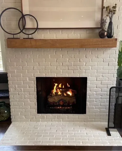 White brick fireplace with a lit fire, wooden mantel, and decorative wall accents in a living room.