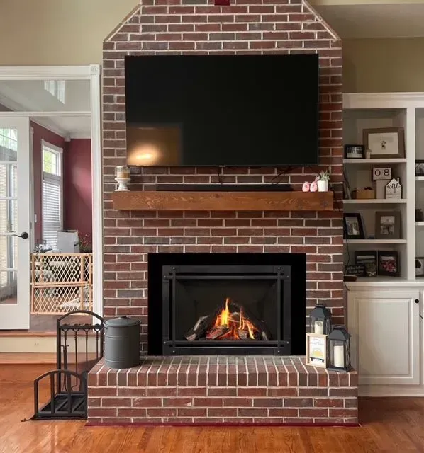 Brick fireplace with lit fire, wall-mounted TV above, and built-in shelves in a living room.