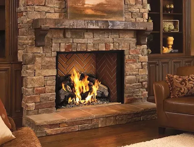 Stone fireplace with a lit fire in a cozy living room, flanked by a leather chair and mantel décor.