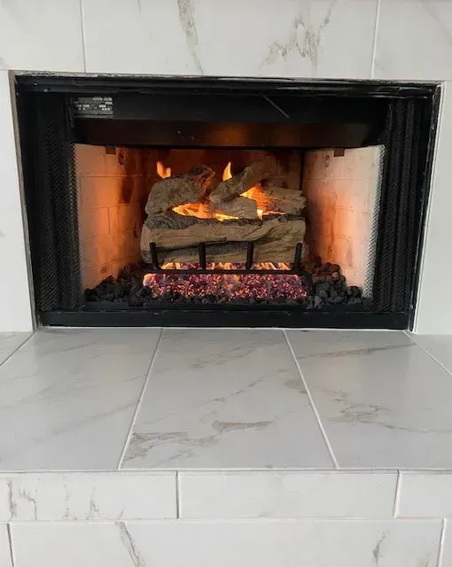 Lit gas fireplace with black frame and white tile surround, flames over stacked logs.