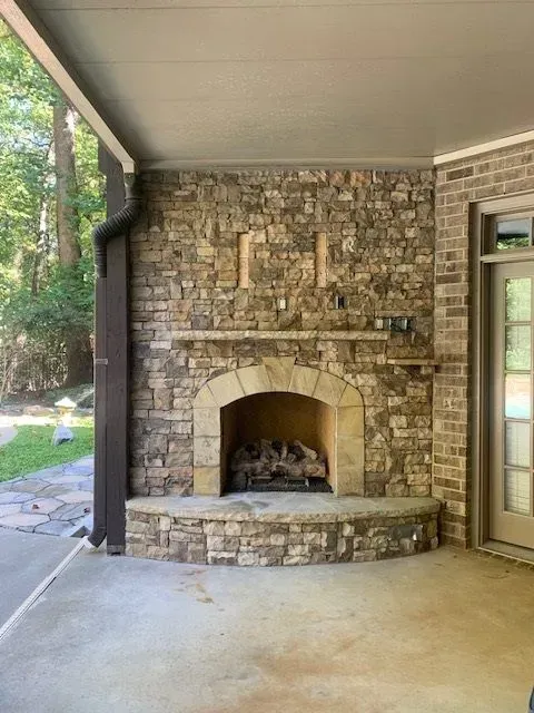 Stone outdoor fireplace under a covered patio with a curved hearth and brick arch opening
