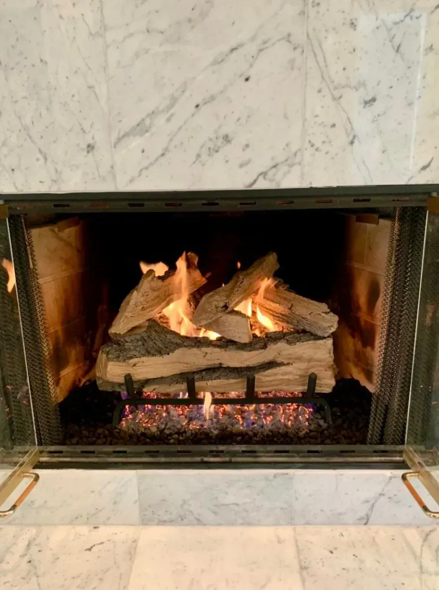 Lit fireplace with orange flames and glowing embers inside a marble hearth.