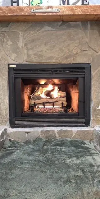 Lit fireplace with flames in a stone hearth beneath a wooden mantel
