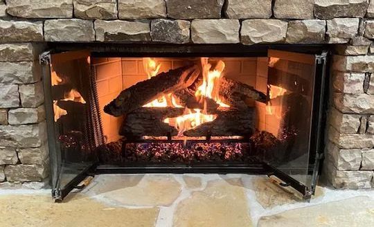 Stone fireplace with a bright burning log fire and black metal screen.