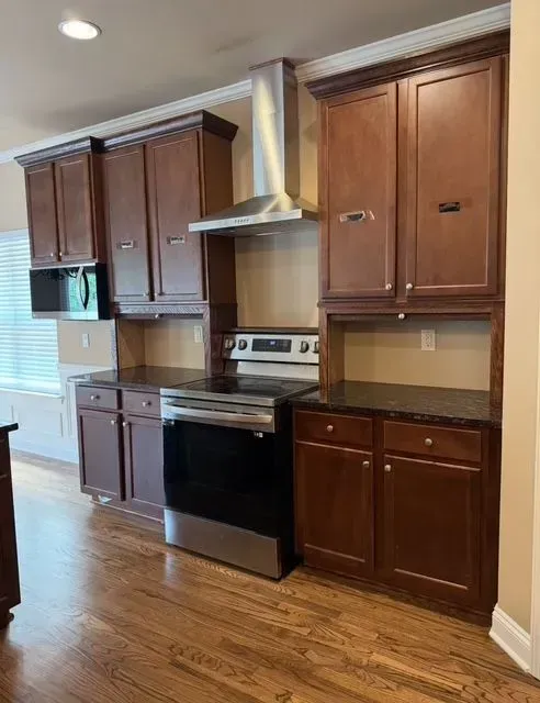 Wooden kitchen cabinets, stainless steel stove, and dark countertops in a bright room with hardwood floors