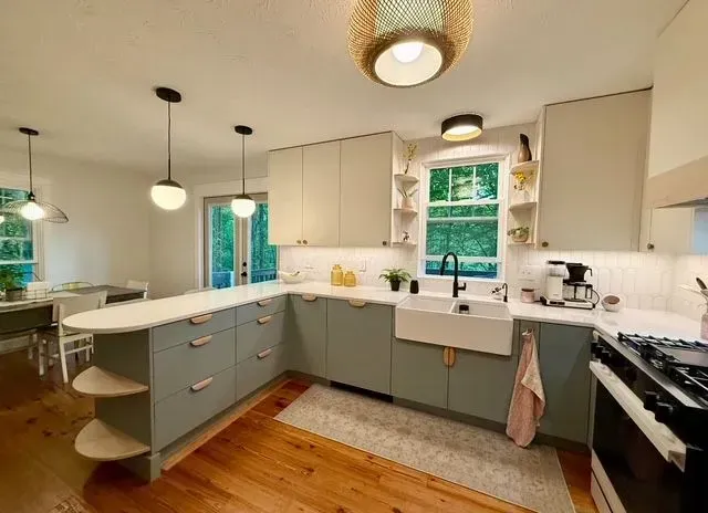 Bright modern kitchen with white cabinets, gray island, wood floors, and green window view