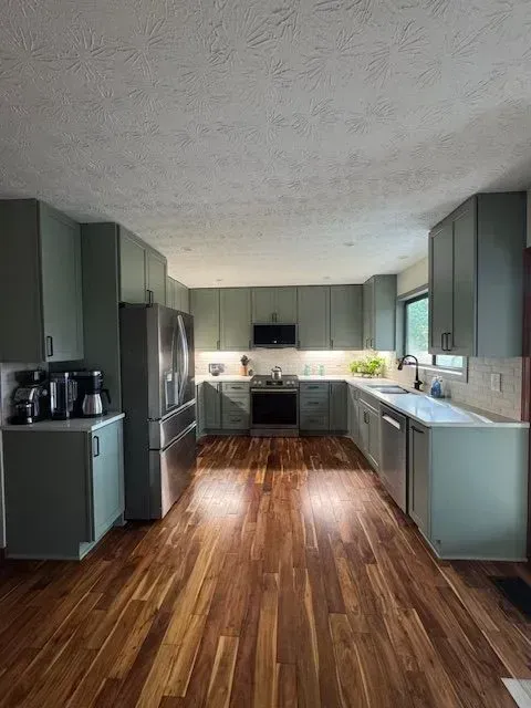 Modern kitchen with sage cabinets, stainless steel appliances, and wood-look flooring
