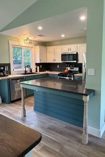 Bright kitchen with blue island, white cabinets, black countertops, and recessed lighting