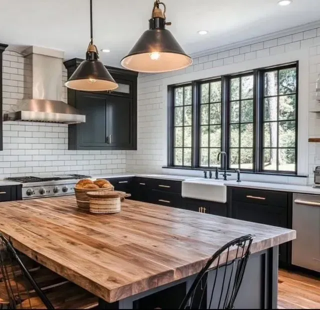 Modern kitchen with black cabinets, white tile, large window, and a wooden island with pendant lights.