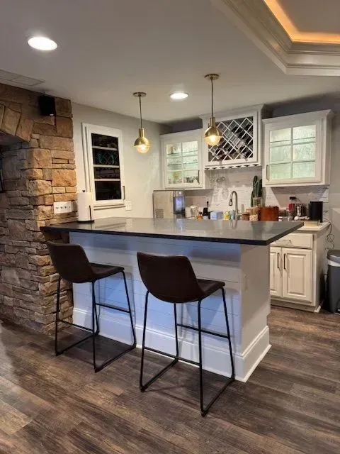Modern kitchen with stone accent wall, white cabinets, dark island, and two bar stools under pendant lights