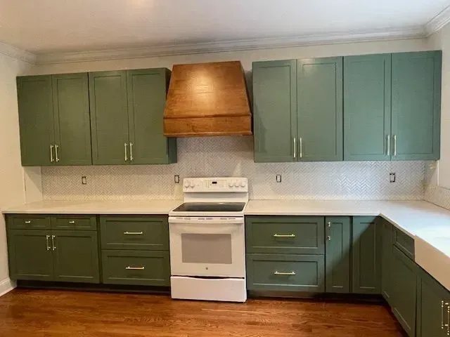 Empty kitchen with green cabinets, white stove, and wooden range hood on a beige tile wall.