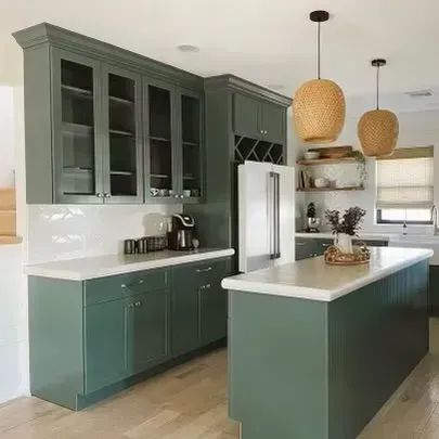 Modern kitchen with sage green cabinets, white countertops, island, pendant lights, and stainless steel refrigerator