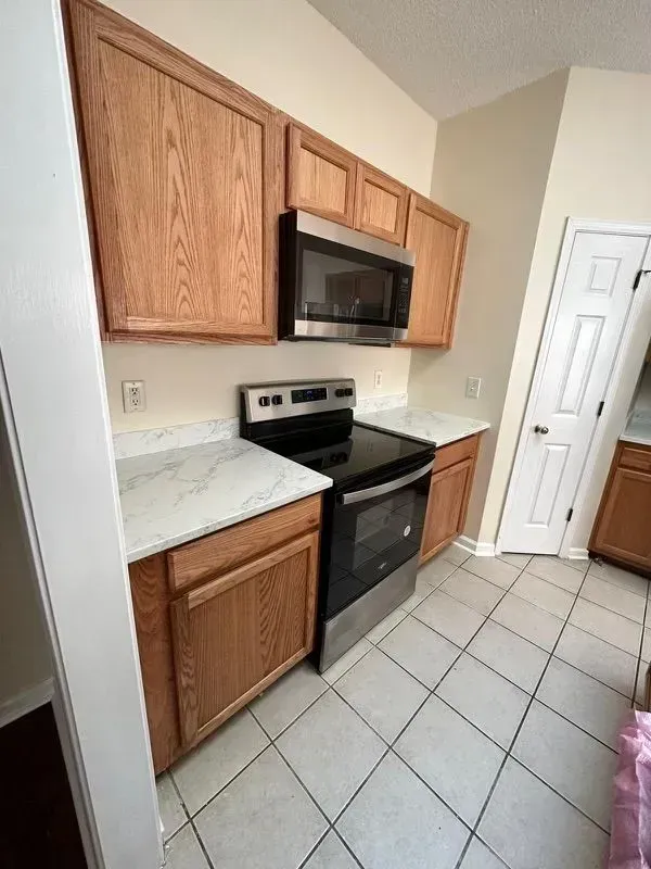 Small kitchen with wooden cabinets, black stove, marble countertop, and tiled floor.