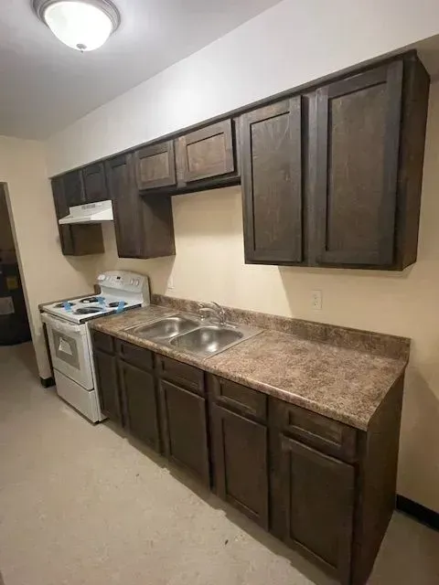 Small kitchen with dark wood cabinets, brown countertops, white stove, and double sink.