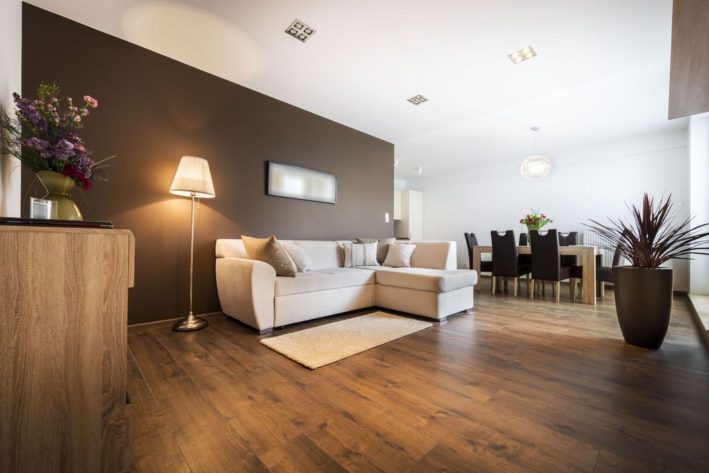 Modern open-plan living room with white sectional sofa, wood floors, and dining area
