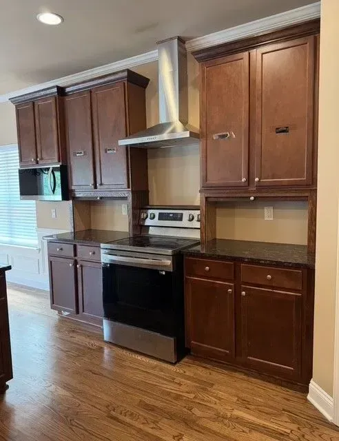 Kitchen with dark wood cabinets, black stove, stainless range hood, and hardwood floor