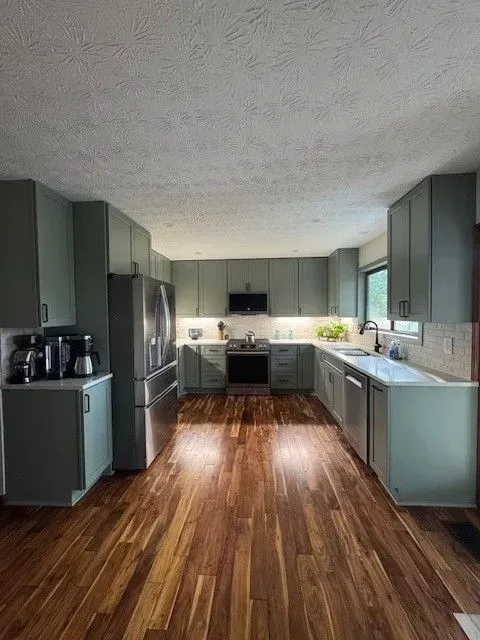 Spacious modern kitchen with sage cabinets, stainless steel appliances, and wood floors.