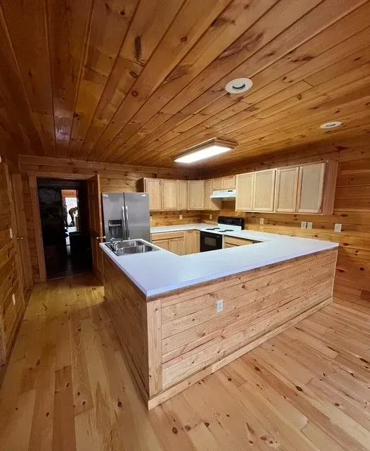 Wood-paneled kitchen with pale cabinets, stainless fridge, white island, and wood floor and ceiling