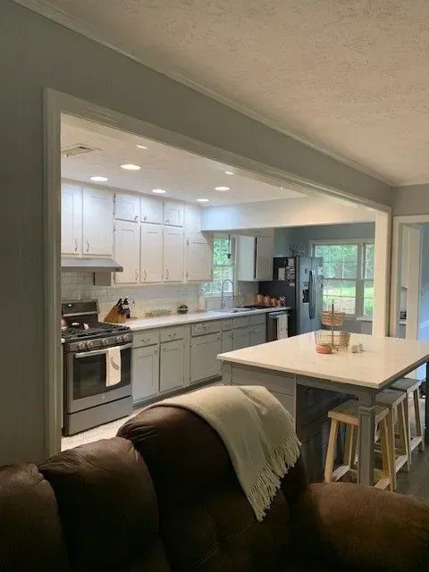 Open kitchen and dining area with white cabinets, island, and brown armchair in foreground