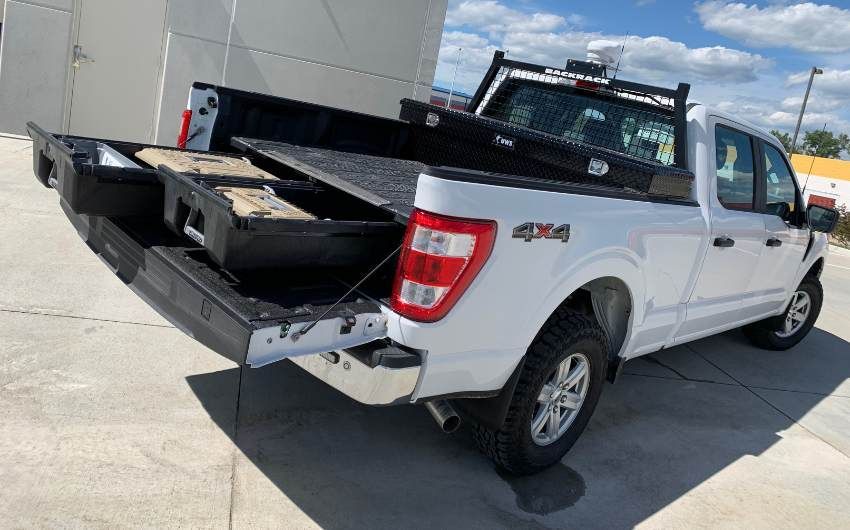 A white pickup truck with the bed open is parked in front of a building.